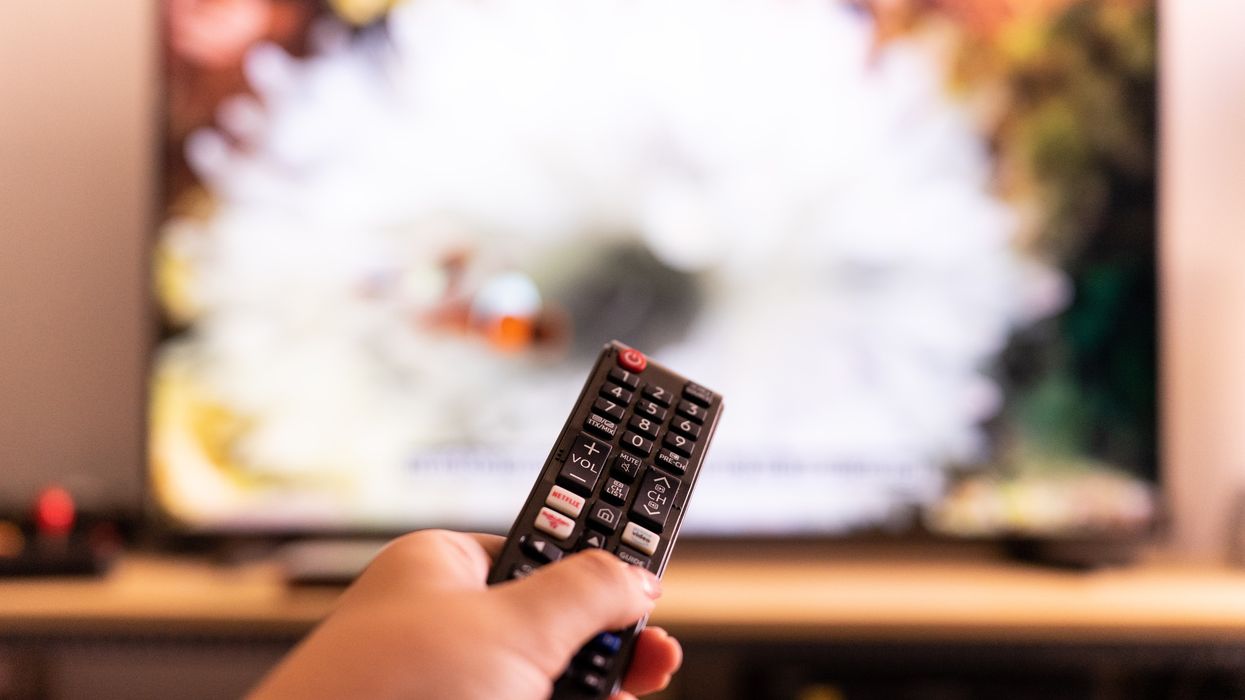 a hand points a remote control at a tv with a blurred image on-screen
