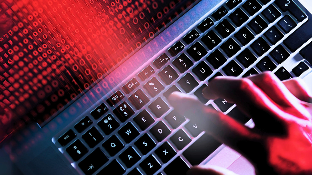 a hand rests on a laptop keyboard with the screen filled with binary code in red