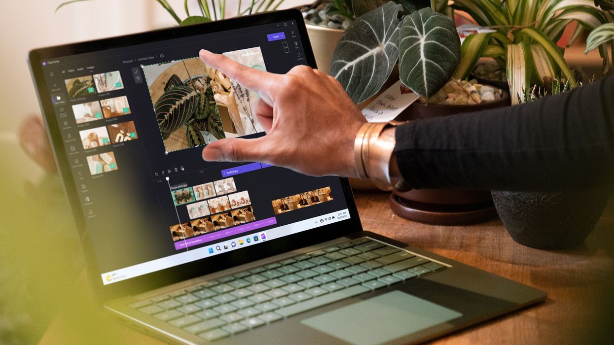 a hand uses the touchscreen on a green microsoft surface laptop 5 running windows 11