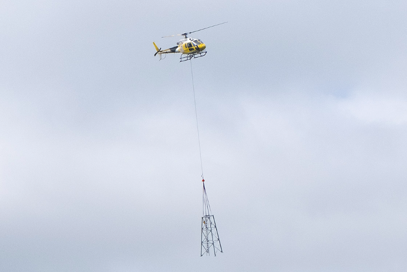 a helicopter is pictured with a piece of a mobile data masts suspended on a wire