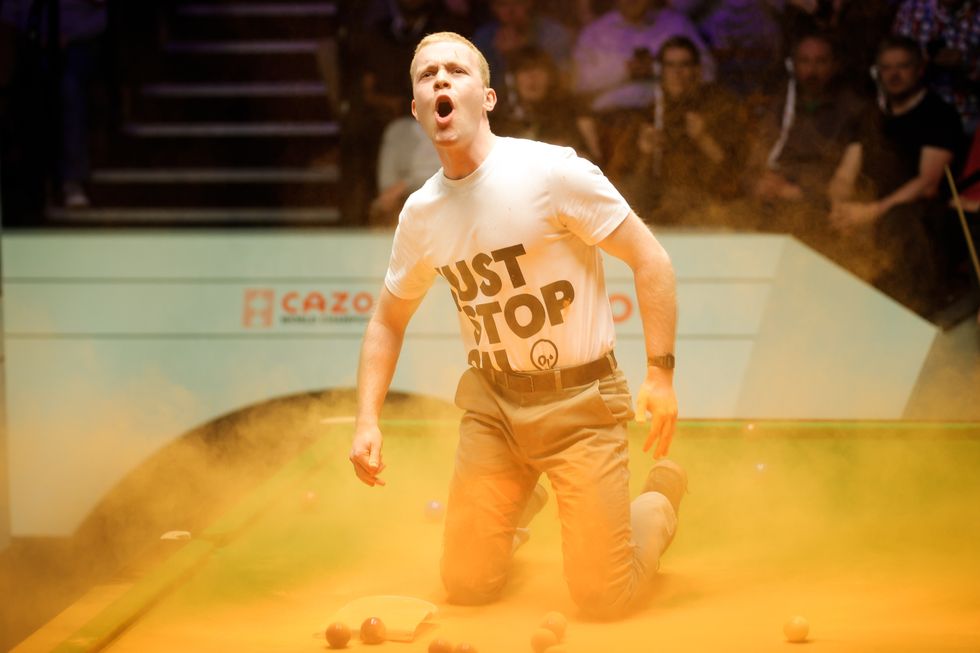A Just Stop Oil protester jumps on the table and throws orange powder 