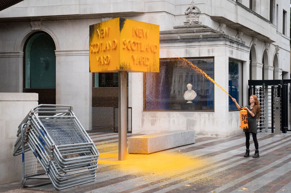 A Just Stop Oil protester spray paints a sign outside New Scotland Yard in London. Picture date: Friday October 14, 2022.
