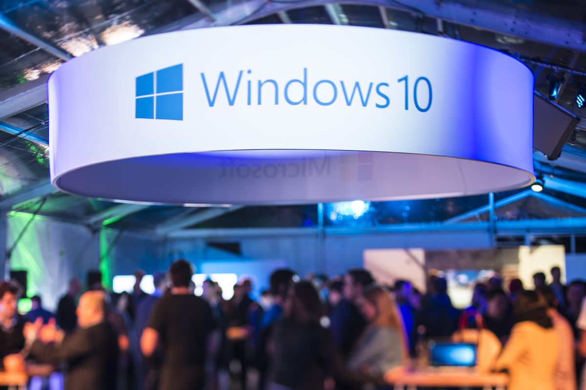 a large banner with windows 10 written on it hangs above a crowded launch party 