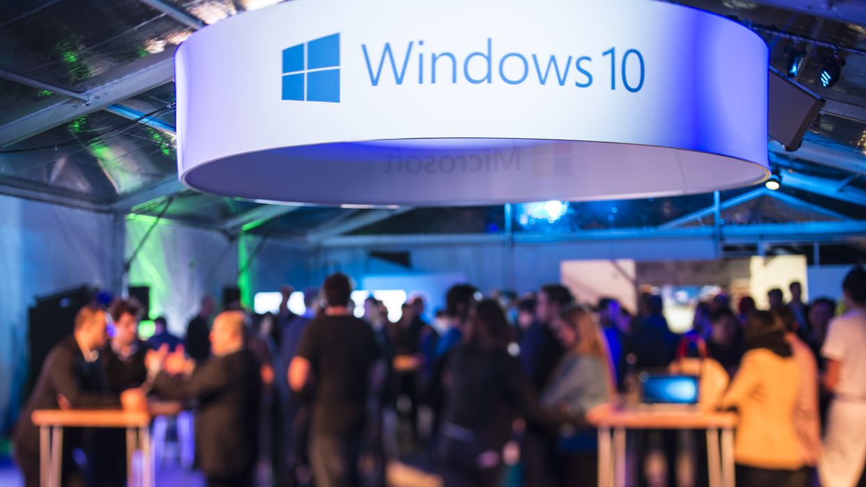 a large banner with windows 10 written on it hangs above a crowded launch party