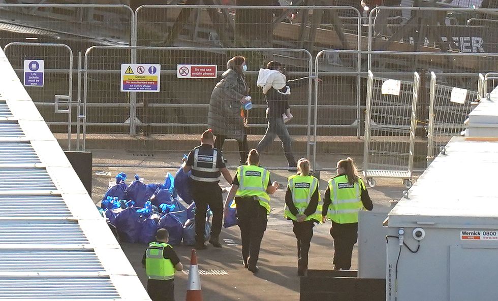 A man carries a young child as a group of people thought to be migrants walk through the Border Force compound in Dover, Kent, after being brought from a Border Force vessel following a small boat incident in the Channel. Picture date: Sunday October 9, 2022.