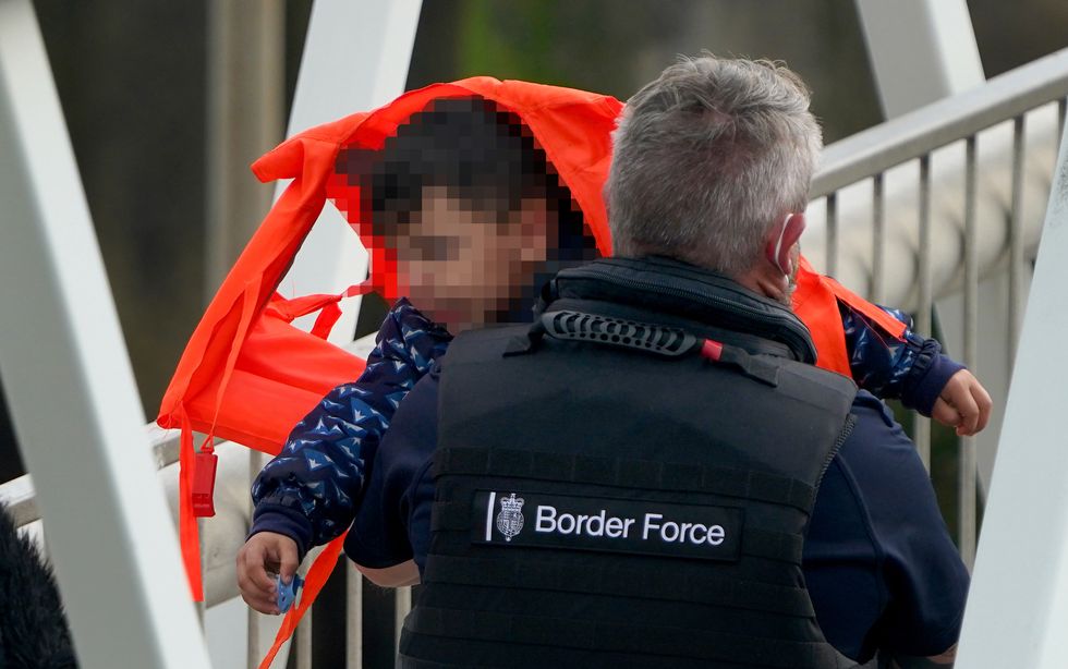 A man carries a young child as group of people thought to be migrants are brought in to Dover, Kent, by Border Force officers, following a small boat incident in the Channel.