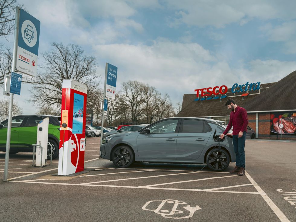 A man charging an electric vehicle outside a Tesco Extra using a Pod Point charger
