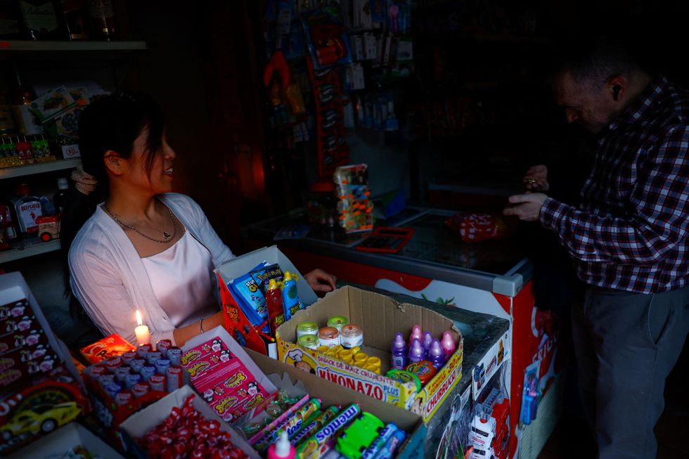 A man has trouble counting coins in low light in a store due to a nationwide power outage in Madrid, Spain