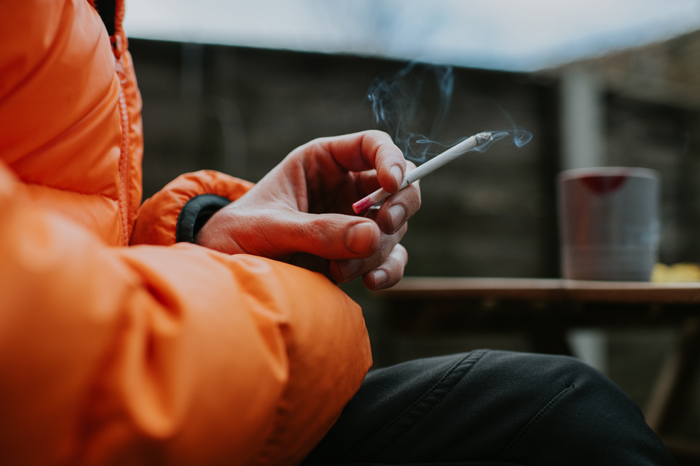 A man holding a cigarette, wearing an orange puffer coat