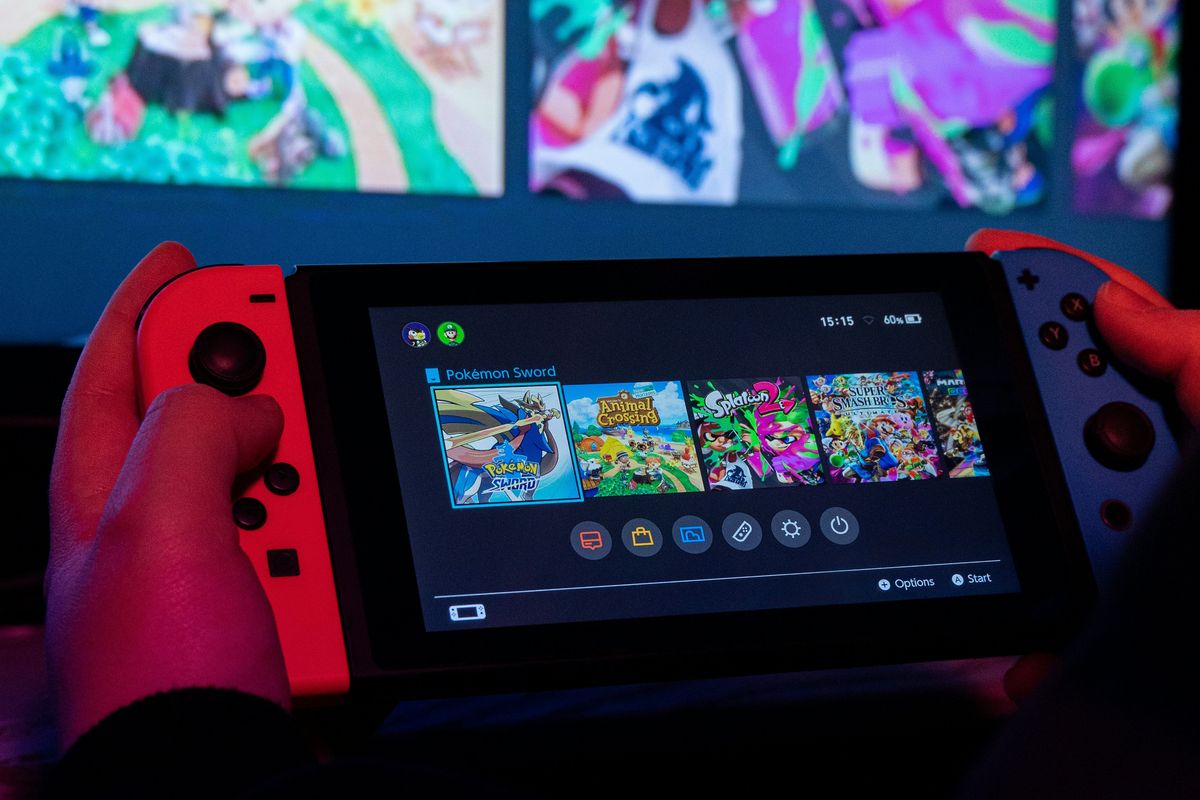 a man holds a nintendo switch with previews of nintendo games like animal crossing and splatoon in the background 