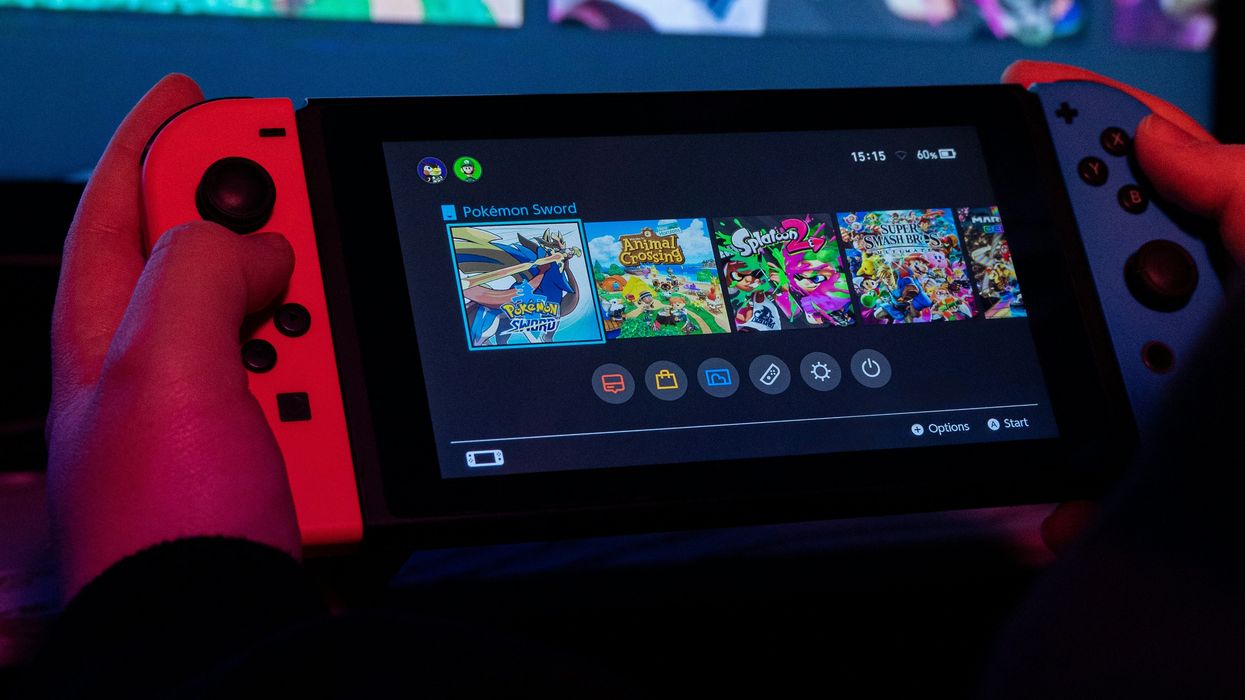 a man holds a nintendo switch with previews of nintendo games like animal crossing and splatoon in the background