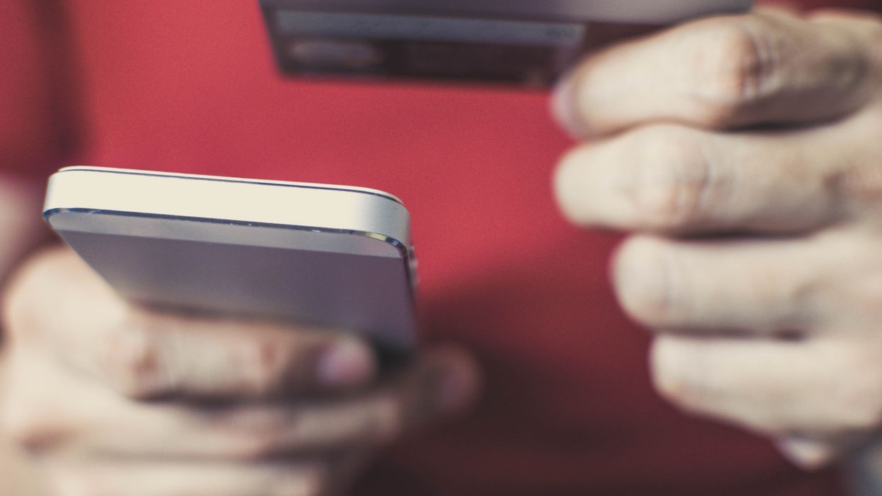 a man holds a smartphone in one hand and a credit card in the other
