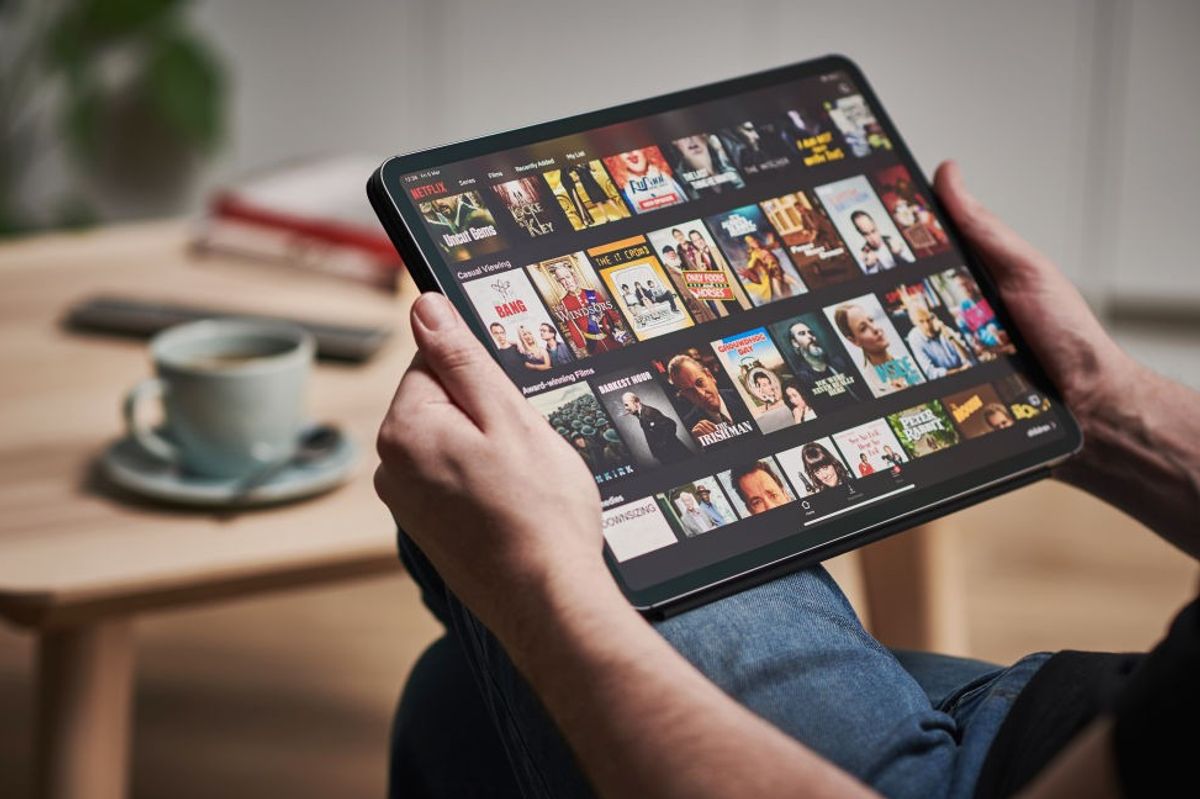 a man holds an ipad with the netflix app showing on screen 