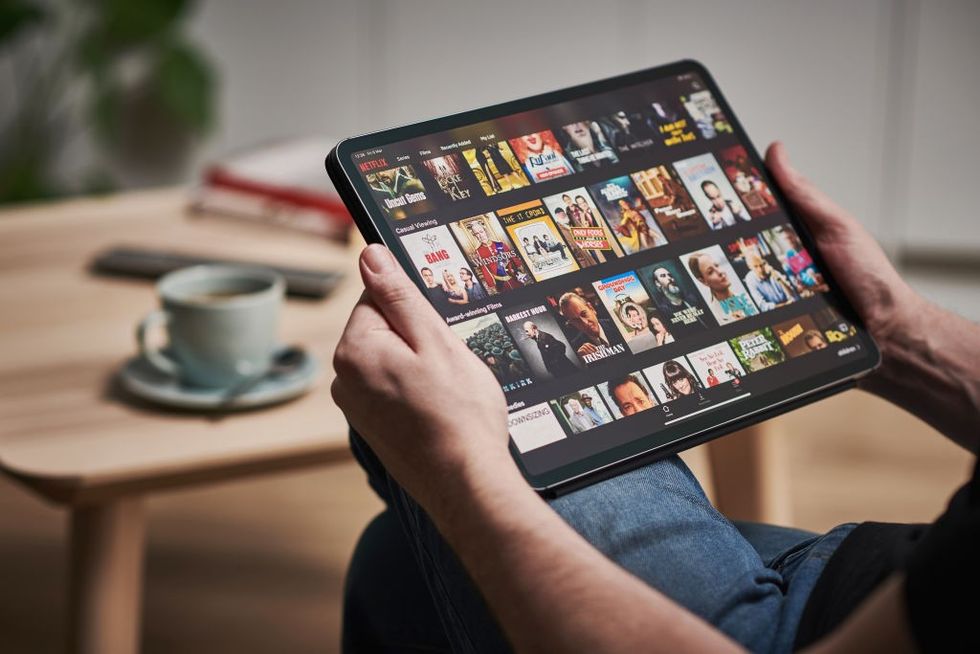 a man holds an ipad with the netflix app showing on screen