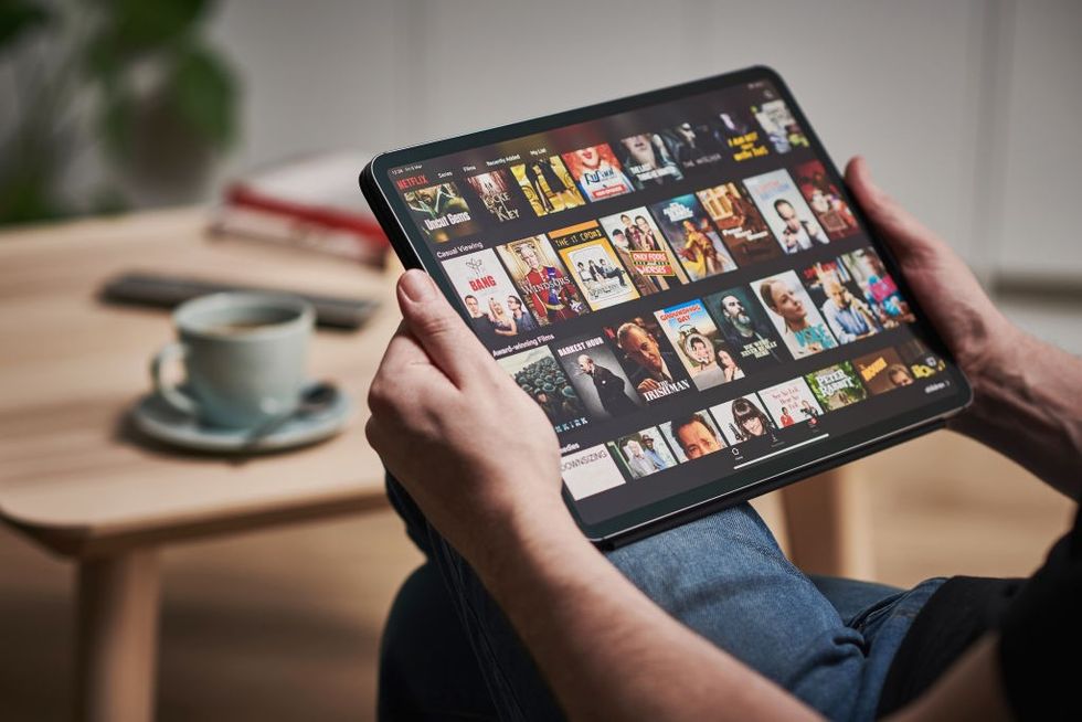 a man holds an ipad with the netflix app showing on screen 
