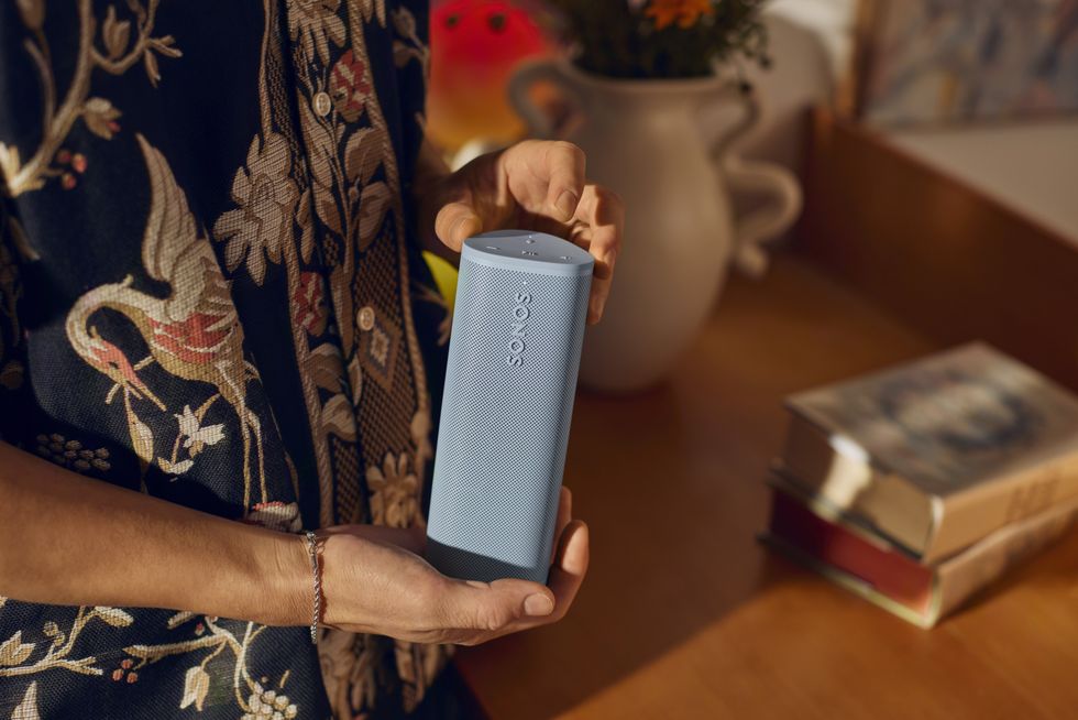 a man holds the sonos roam 2 speaker in blue