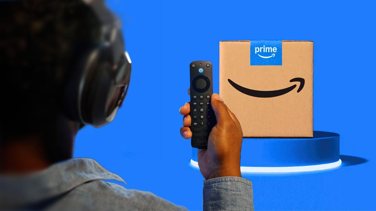 a man holds up the fire tv stick alexa pro remote with a prime delivery box seen in the background