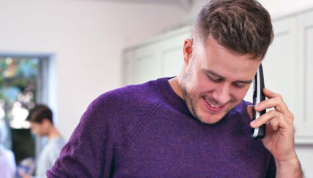 a man in a purple jumper makes a call on a BT Digital Voice wireless handset