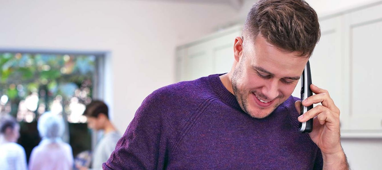 a man in a purple jumper makes a call on a BT Digital Voice wireless handset
