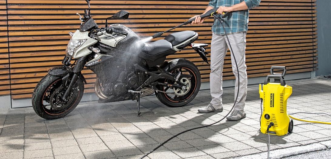 a man is pictured using a bright yellow karcher pressure washer to clean a motorcycle on the driveway