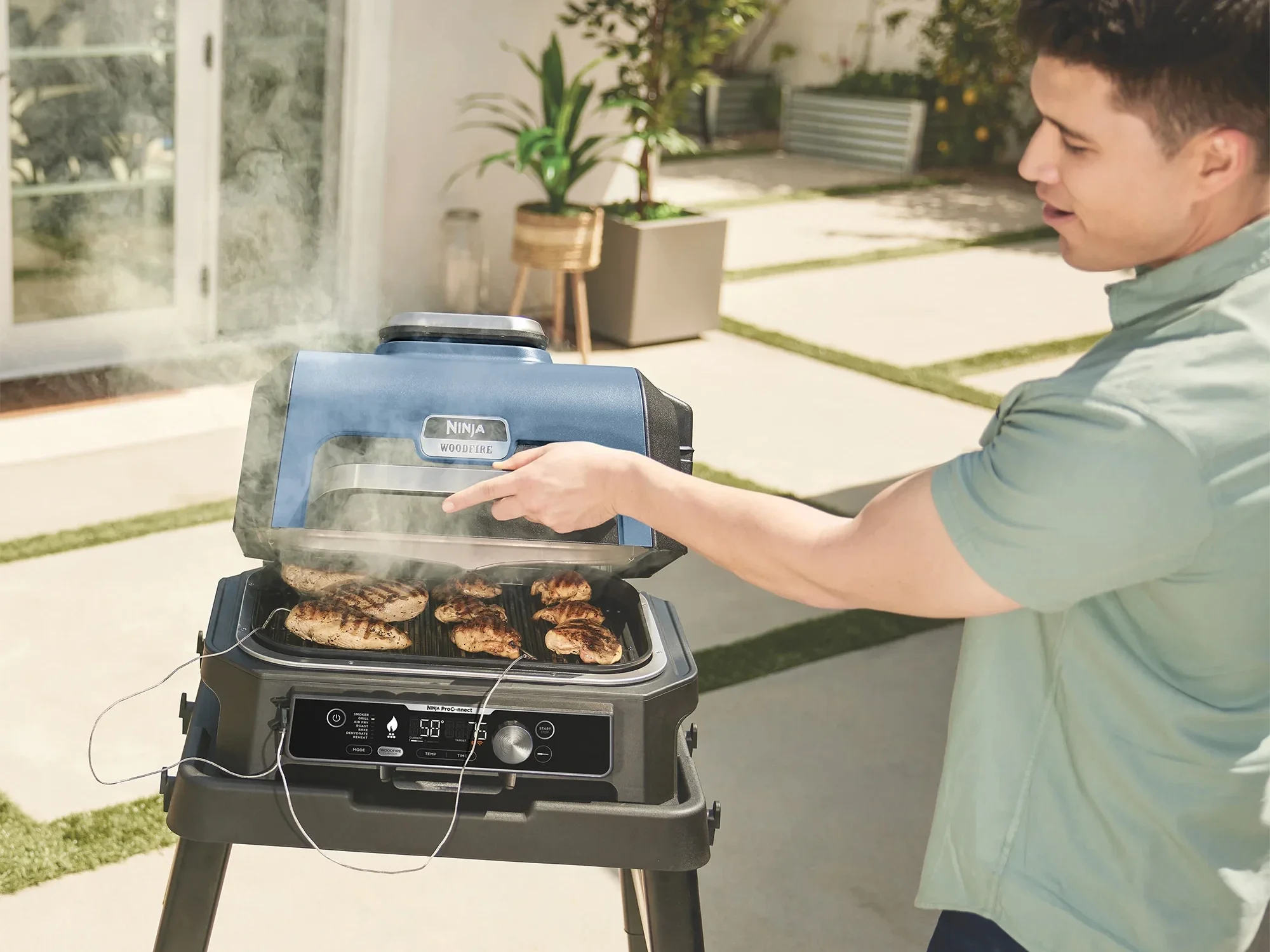 a man opens the ninja bbq woodfire oven and looks at the temperature probes in the chicken
