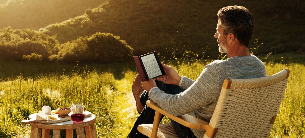 a man reading a kindle paperwhite outside in a field