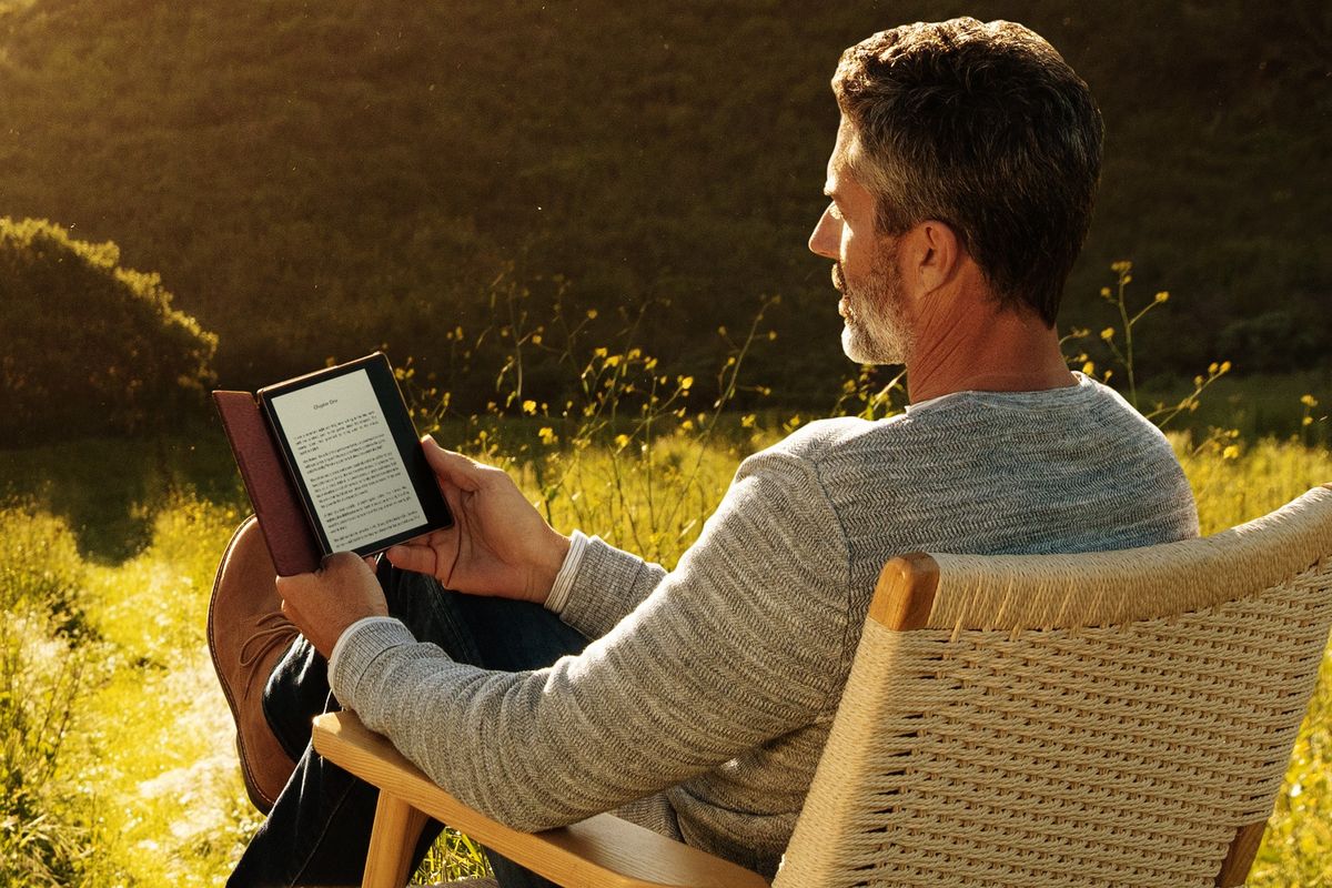 a man reads on his Kindle e-reader outside in a chair with the backlight on outdoors on a camping trip  