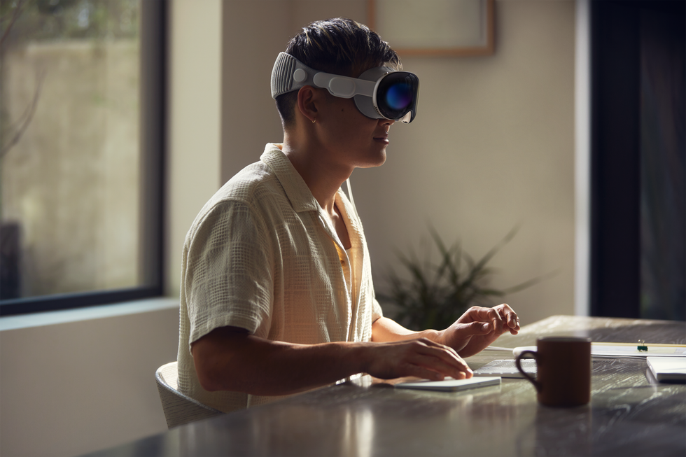 a man sits at a desk typing on a keyboard with a mouse using the vision pro