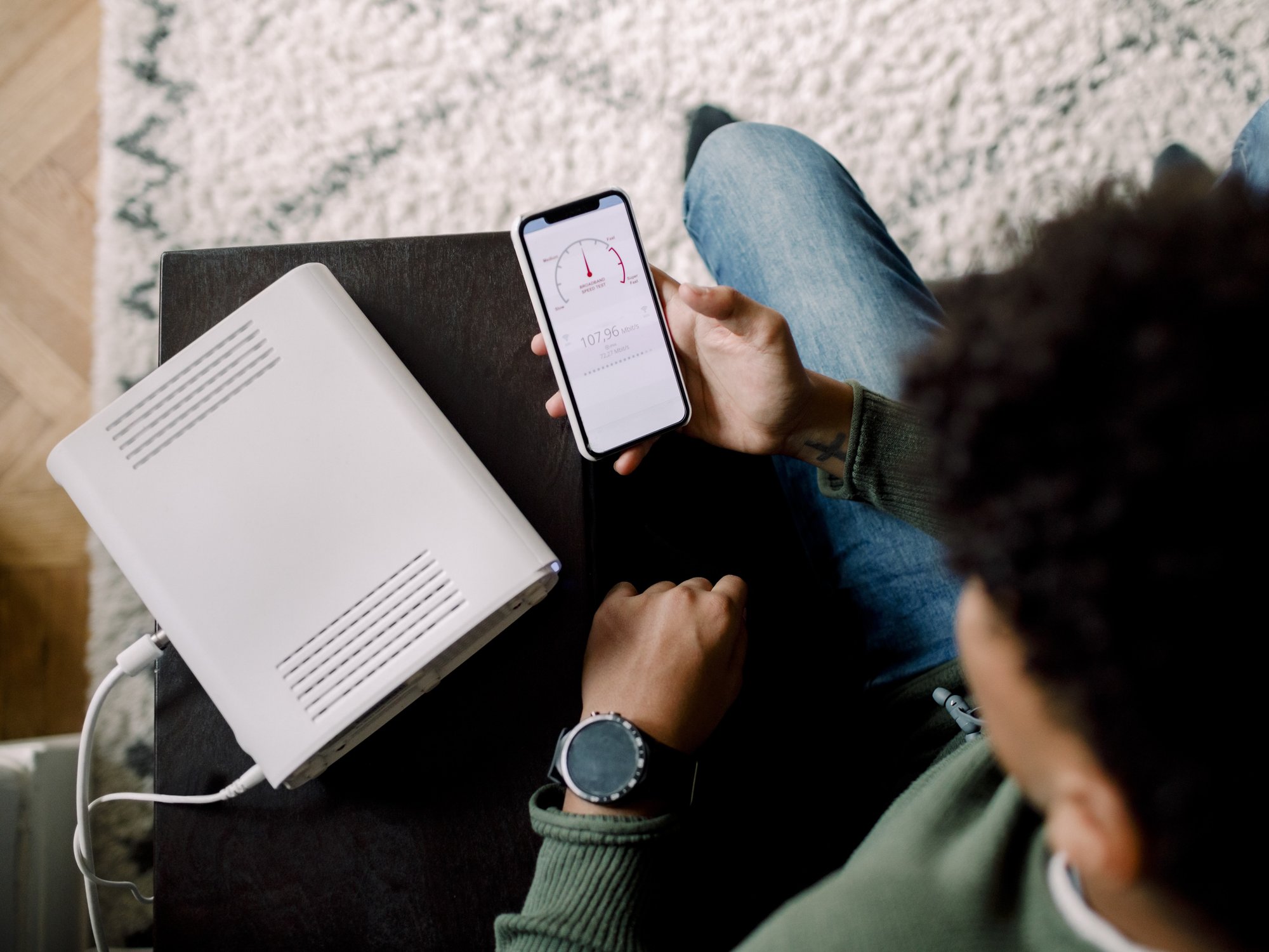 a man sits next to his broadband router and runs a speed test on his phone