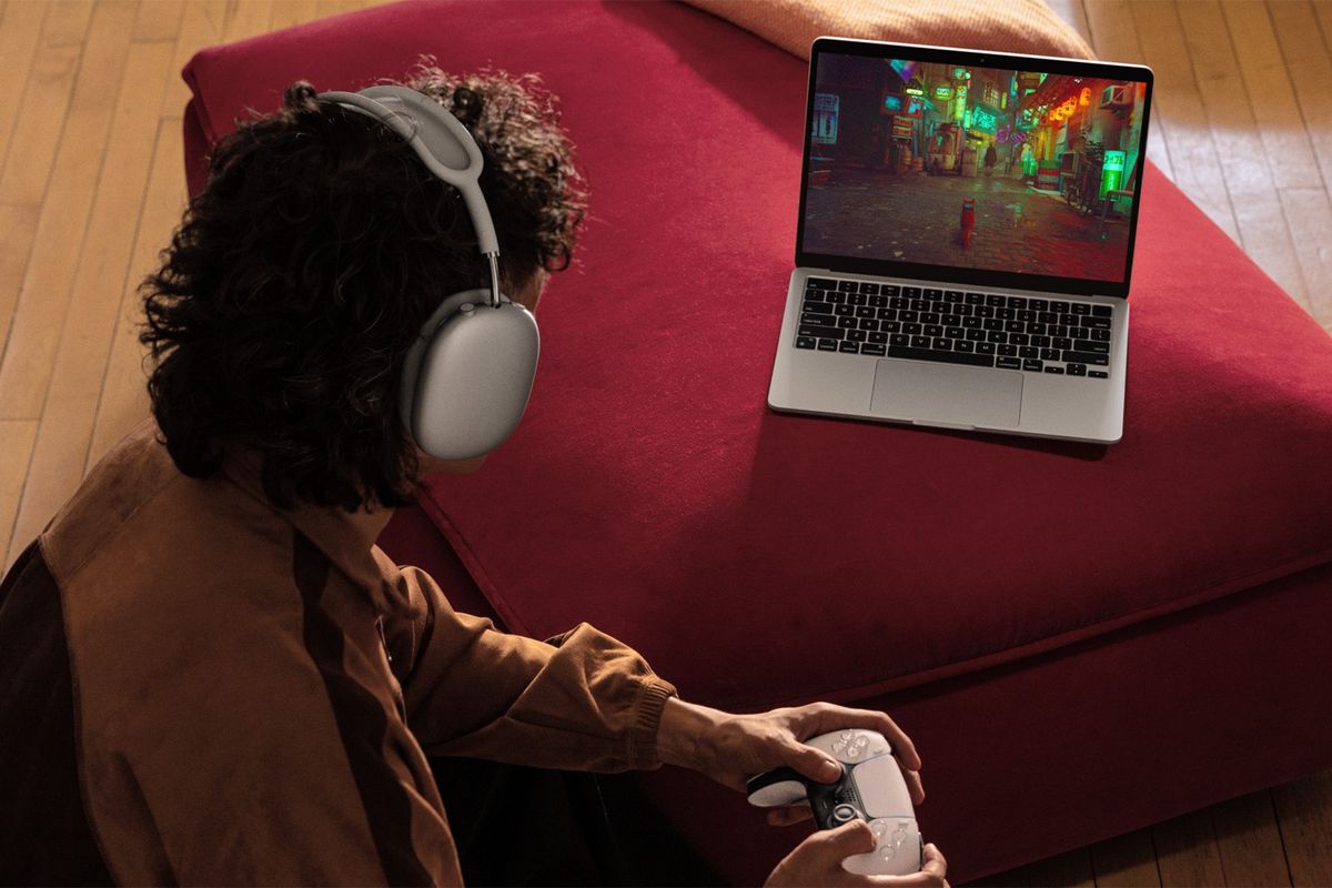 a man sits with airpods pro and a ps5 controller playing games on a macbook air m3