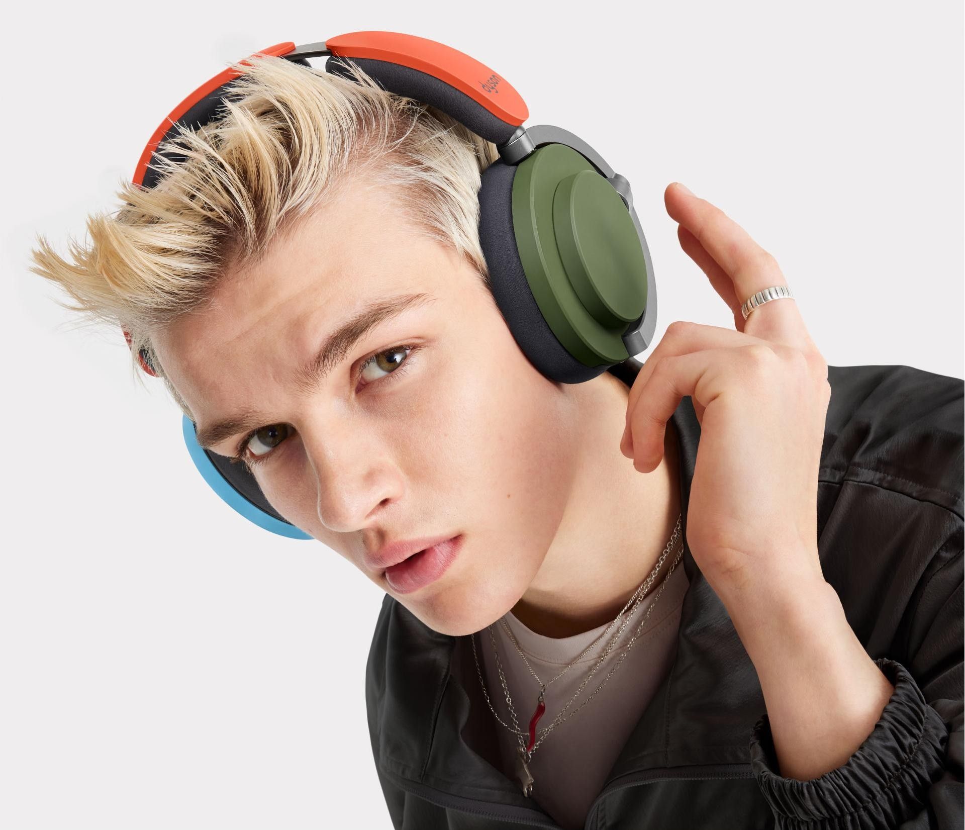 a man taps the earcup of the Dyson OnTrac with one green and one blue exterior cup and an orange headband that's been customised