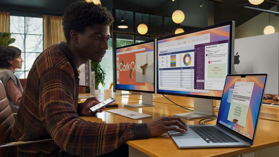 a man uses the trackpad on the macbook air with two external displays running multiple apps from the laptop