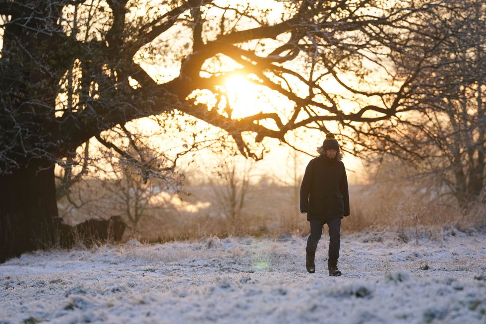 A man walks across wintry ground during sunrise in Priory Park in Warwick