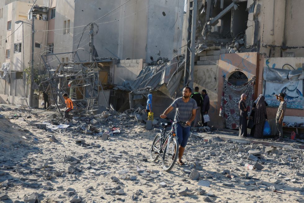 A man walks along with a cycle as Palestinians inspect the site of Israeli strikes on houses in Khan Younis in the southern Gaza Strip