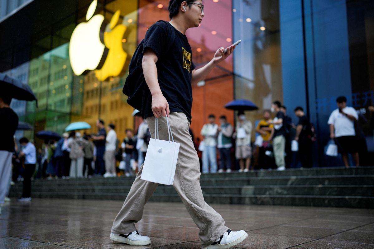 a man walks outside of an apple store with a branded shopping bag 