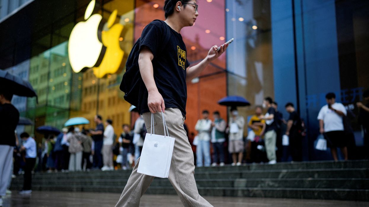 a man walks outside of an apple store with a branded shopping bag