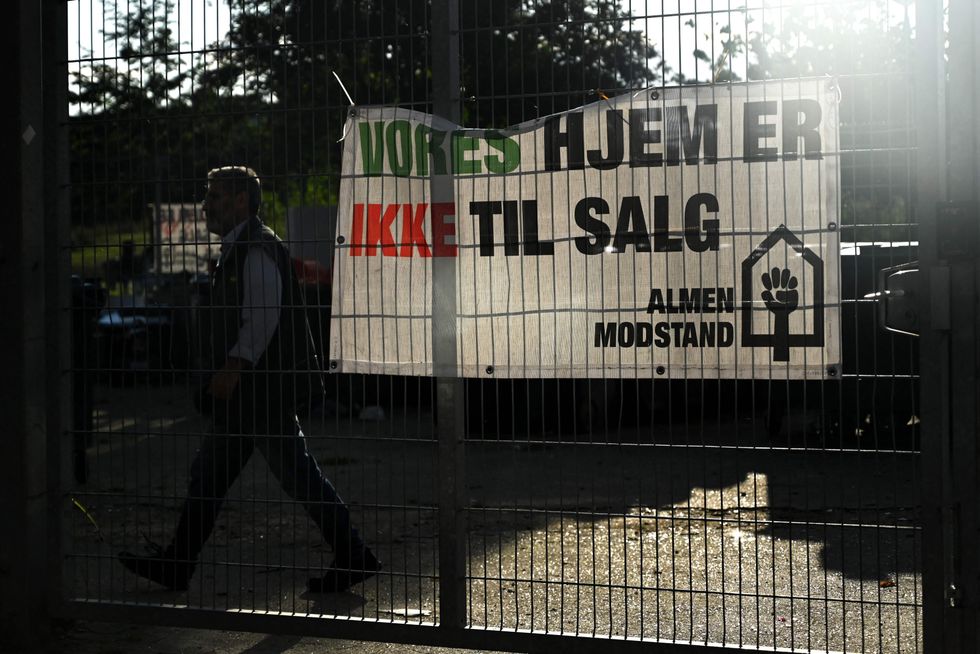A man walks past a banner with a text reading 'Our homes are not for sale' in the courtyard of Mjolnerparken housing estate in Copenhagen