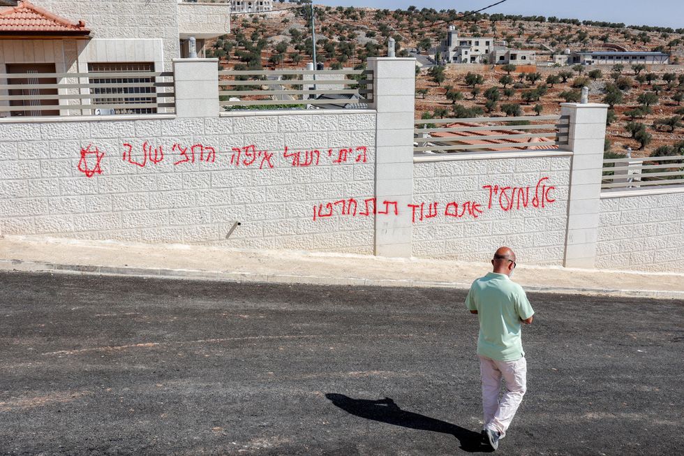 A man walks past Hebrew graffiti reading "Al-Mughayyir, you will regret" reportedly painted by Israeli settlers on a Palestinian home following an overnight attack on the Palestinian Christian village of Taybeh