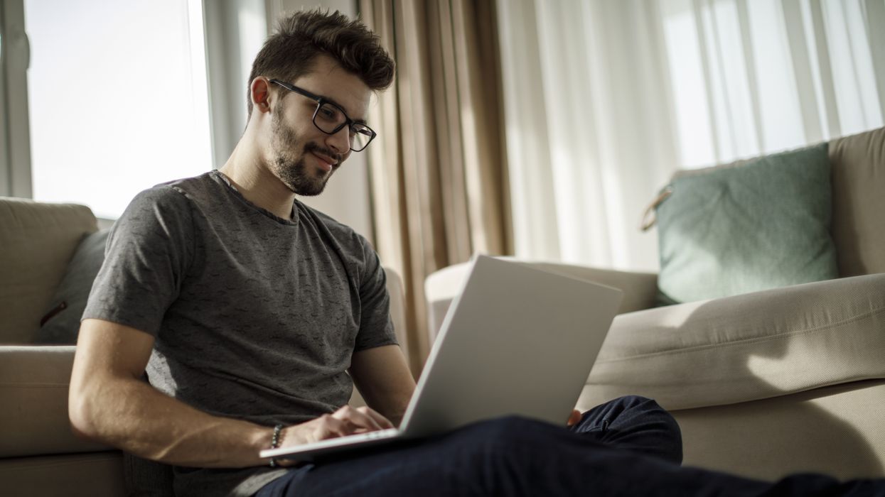 a man with glasses sits on the floor with a laptop on his knees