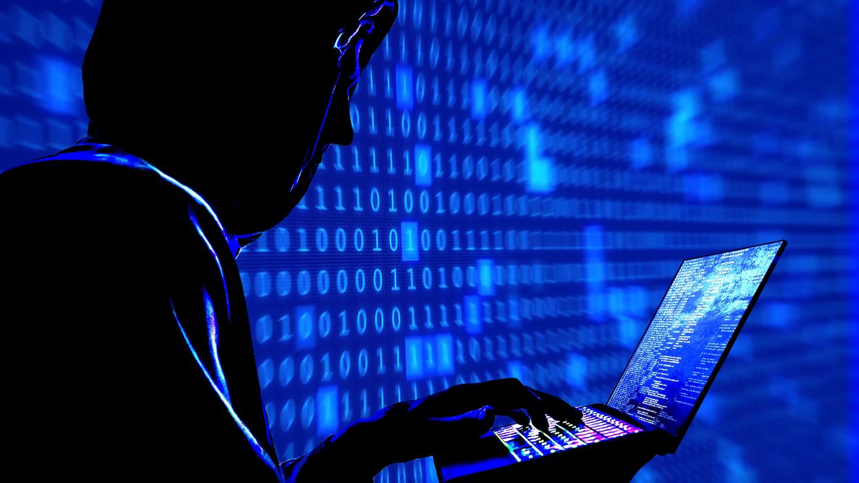 a man with his hood pulled up is pictured typing on a laptop with a blue background of code