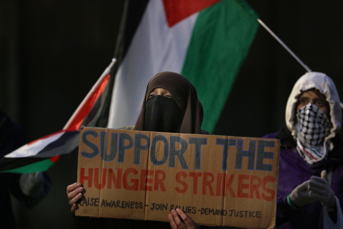 A masked protester holds a sign in support of the hunger strikers
