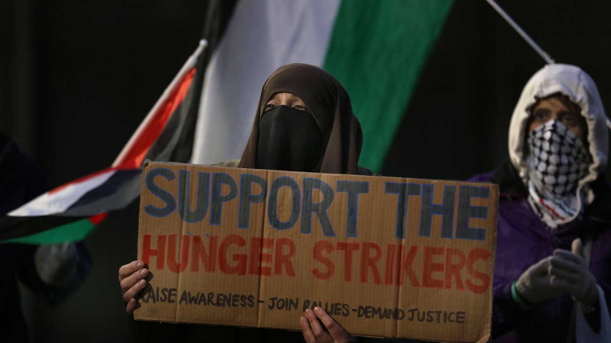 A masked protester holds a sign in support of the hunger strikers