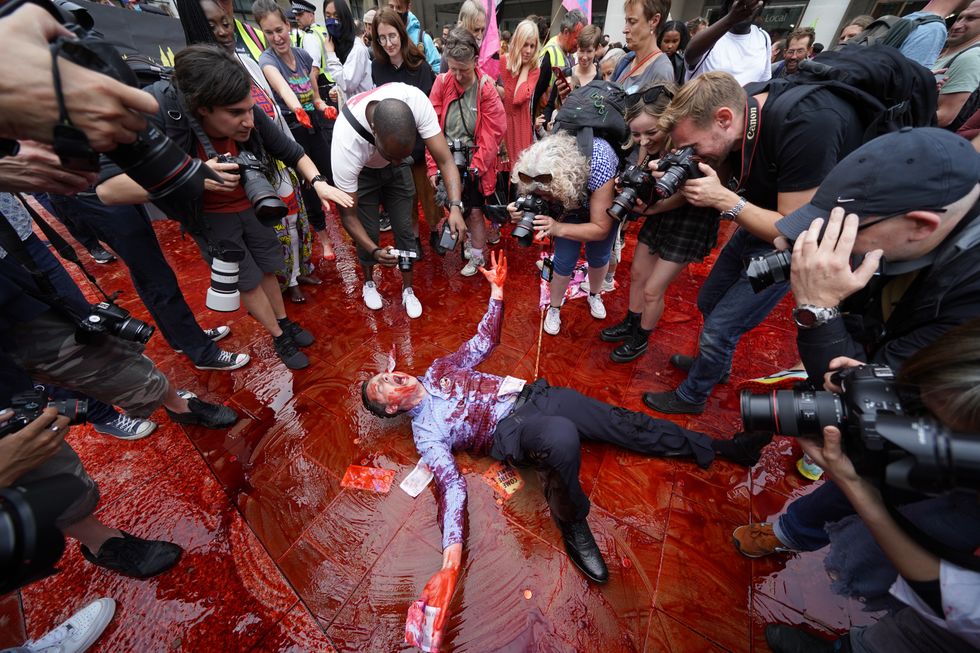 A member of Extinction Rebellion rolling around in fake blood in Paternoster Square, central London. Picture date: Friday August 27, 2021.