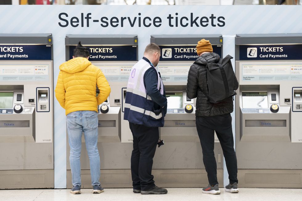 A member of staff assists a person at the ticket machines in Waterloo Station train station in London