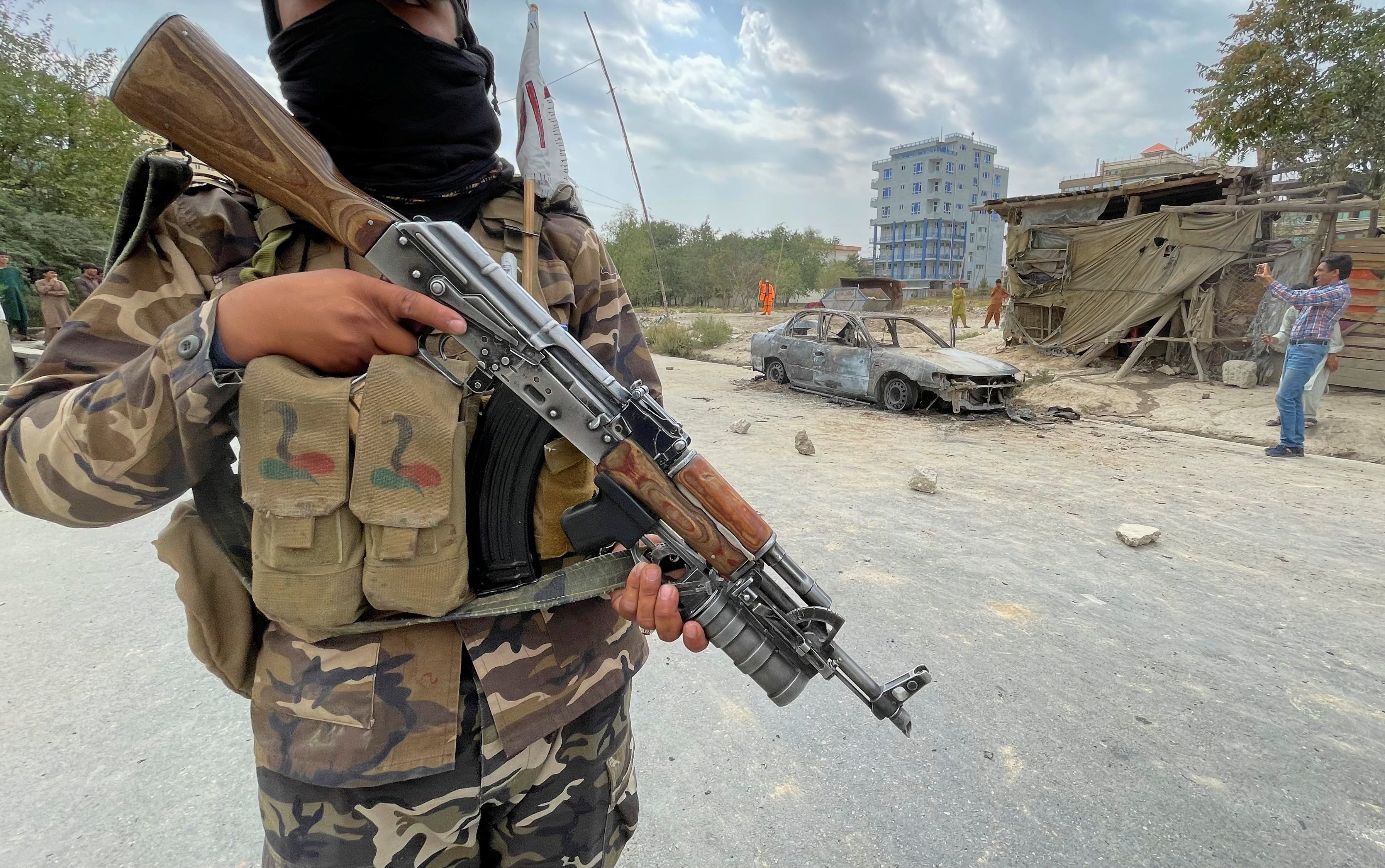 A member of Taliban forces stands guard as Afghan men take pictures of a vehicle from which rockets were fired, in Kabul.