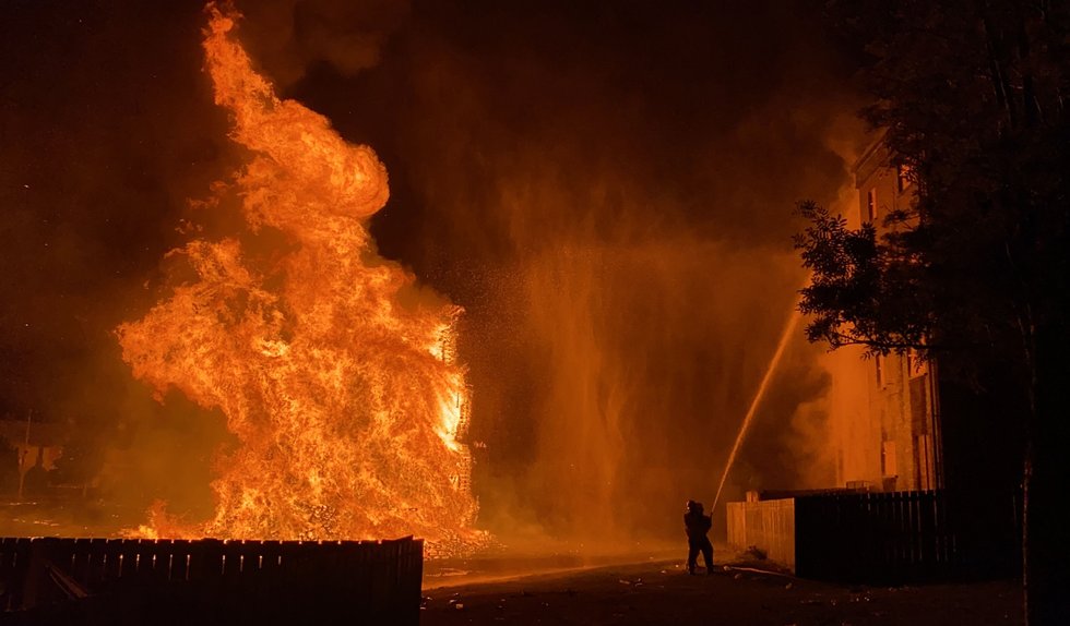 A member of the Fire Service dampens down nearby flats as huge bonfire burns in the loyalist Corcrain area of Portadown.