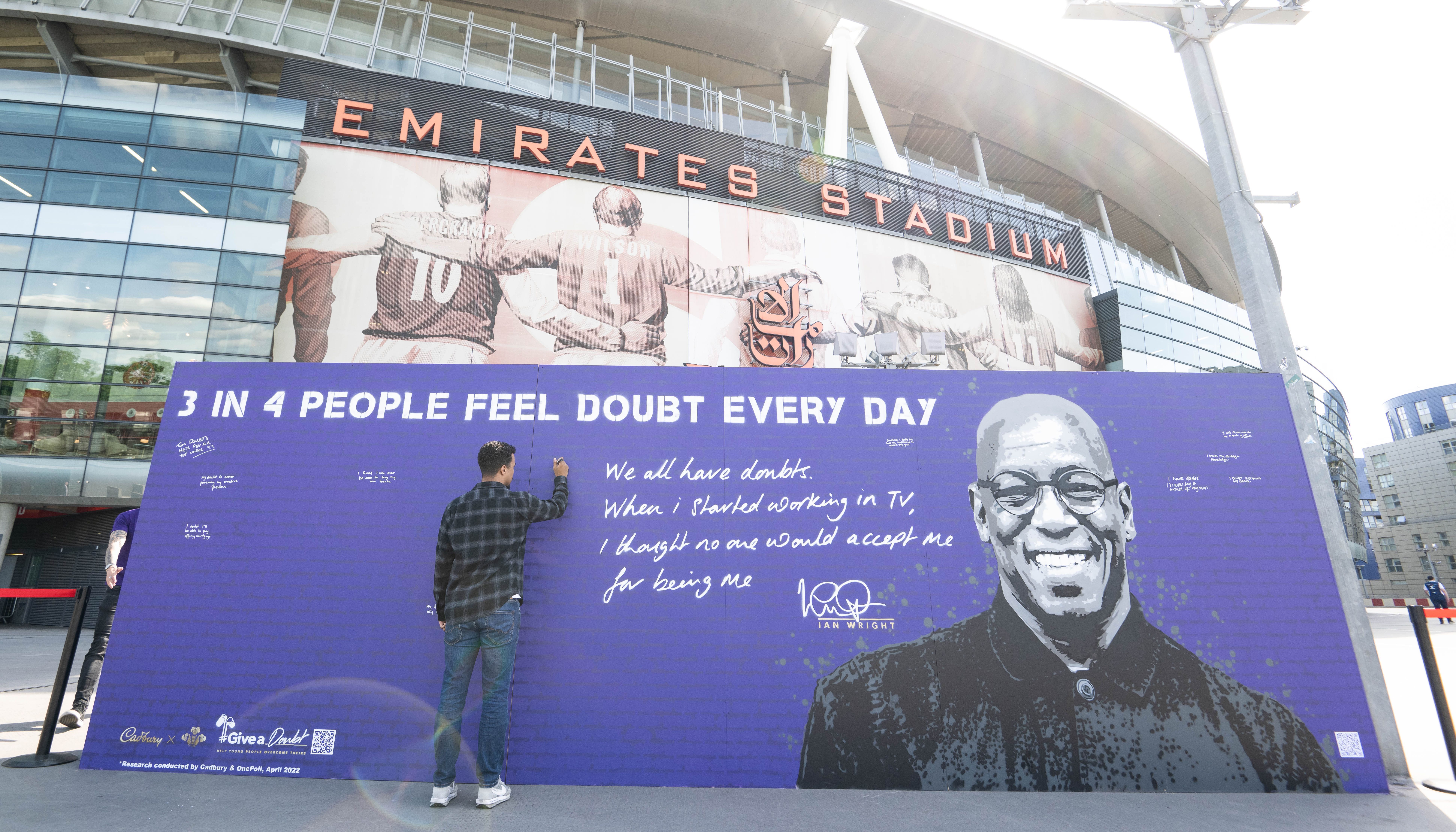 A member of the public writes on the Cadbury Wall of Doubt at The Emirates stadium in London