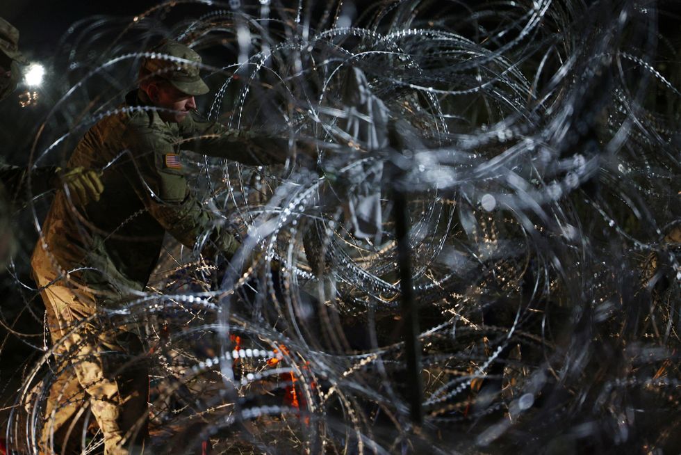 A member of the Texas National Guard reinforces the razor wire to keep out a large group of migrants