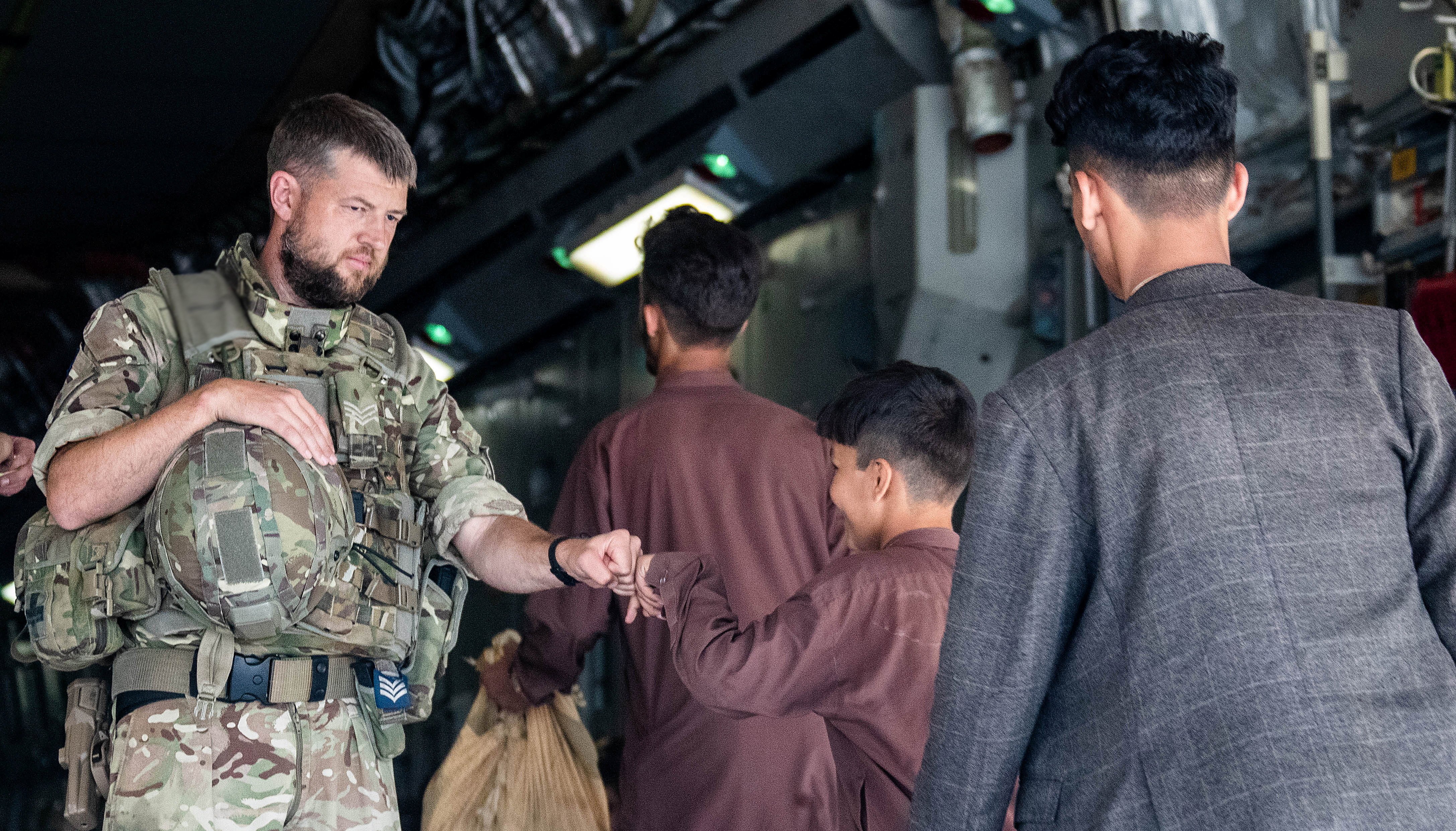 A member of the UK Armed Forces bumps fists with a child as he continues to take part in the evacuation of entitled personnel from Kabul airport.