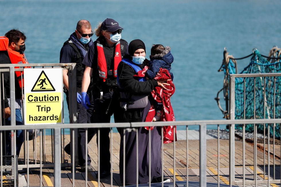 A migrant, rescued from the English Channel, walks holding a child in Dover